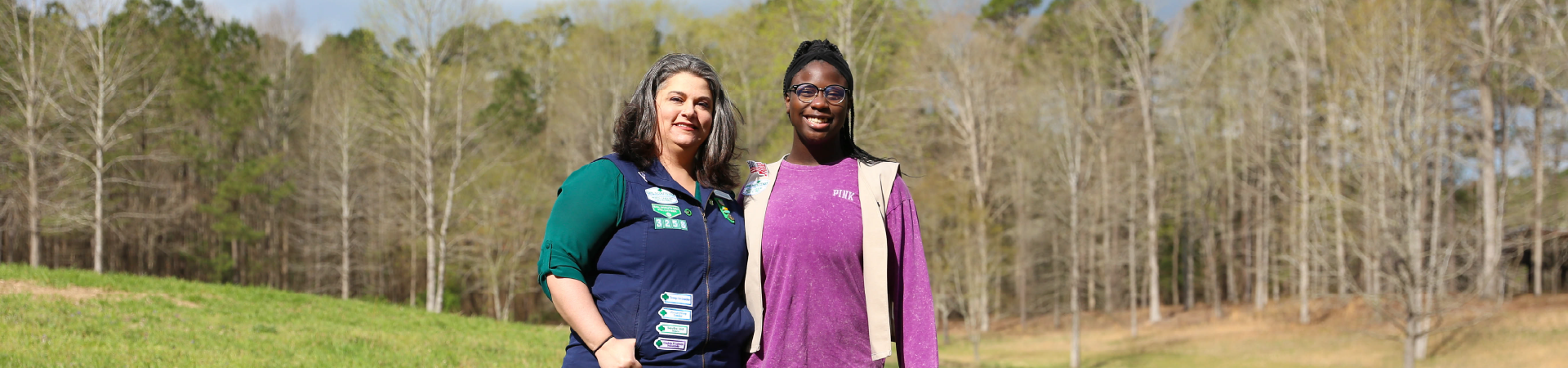  older Girl Scout and Troop Co-Leader pose in wooded area 