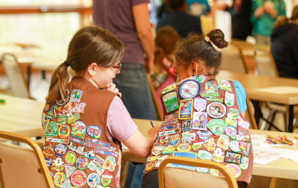 two Brownies with badges and patches all over their vests lean over and color