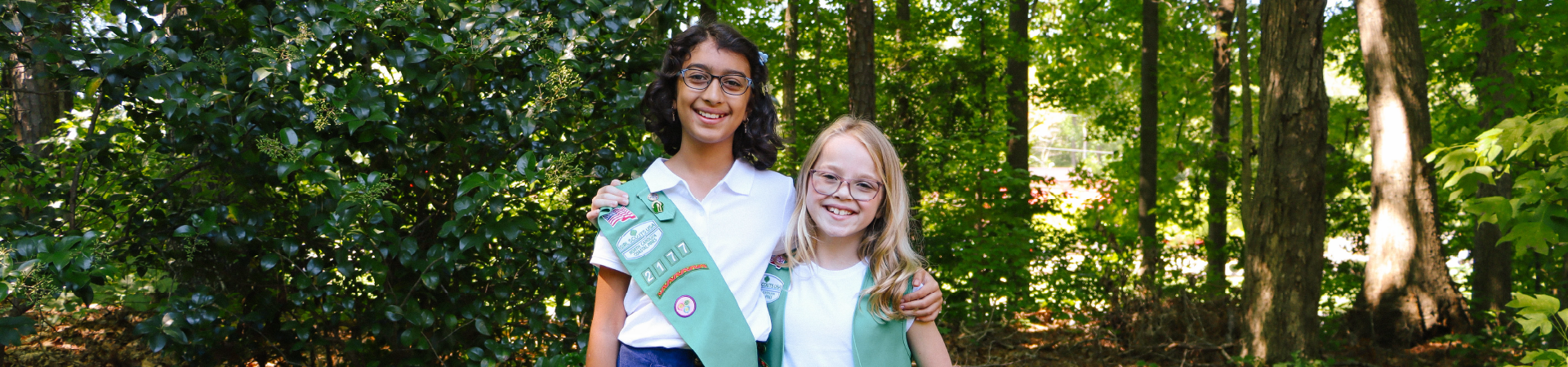  two Girl Scouts smile together near forest 