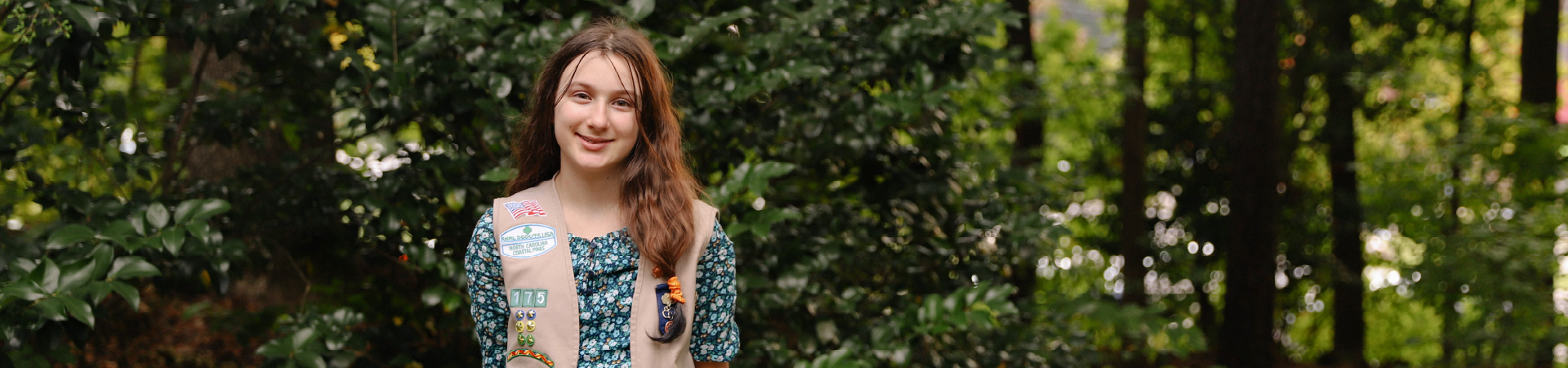  Girl Scout smiling at the camera in front of a bush 