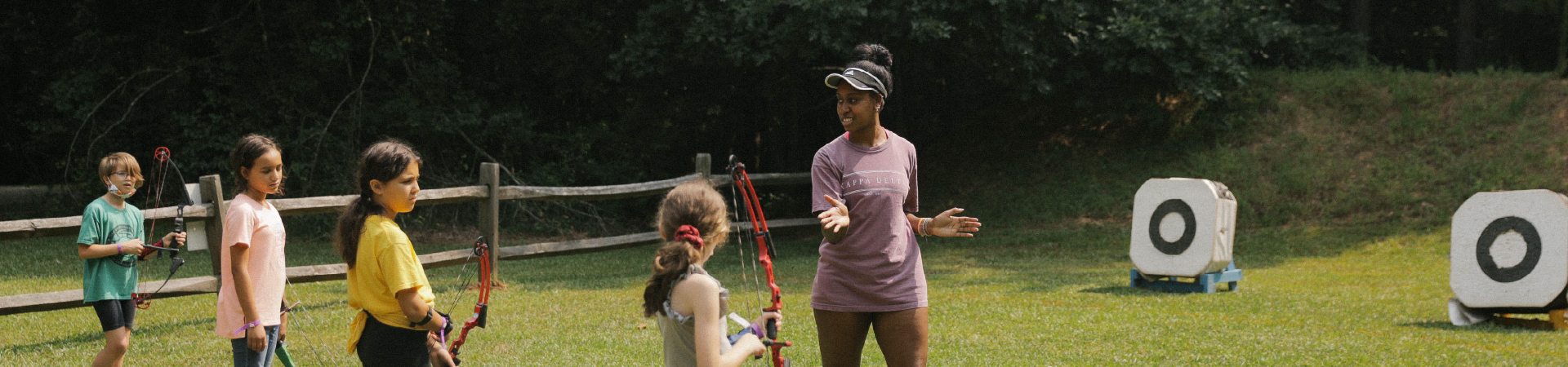  camp staff instructs young girls in archery 