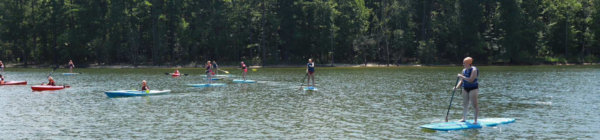  group of Girl Scouts paddling on paddle boards in a lake 