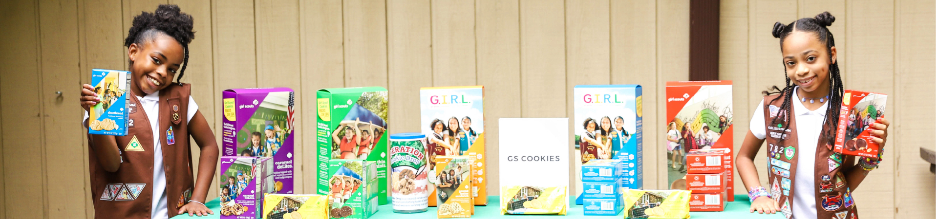  girl scout wearing uniform on either side of a cookie booth 