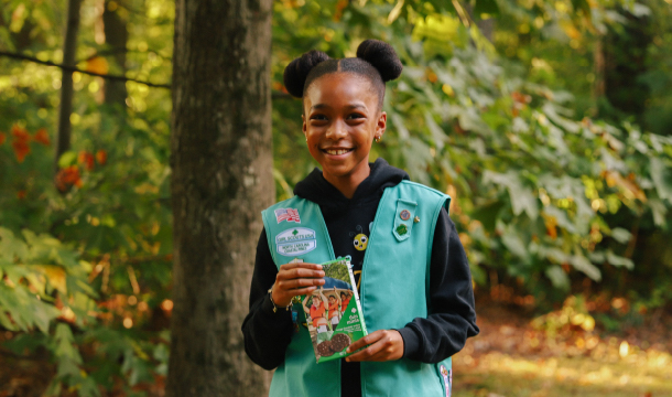 Girl Scout in hoodie and Junior vest shows off a box of Thin Mints