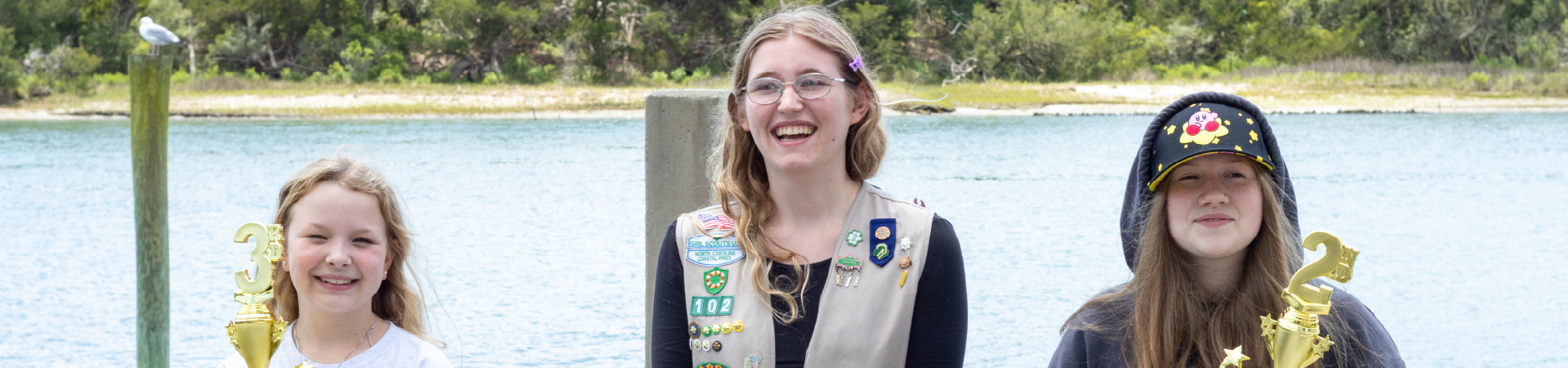  three girl scouts holding awards celebrate in front of lake 
