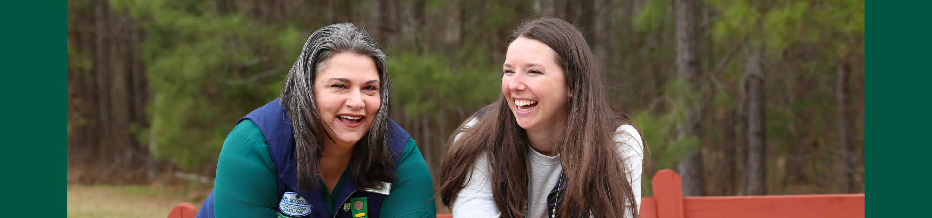  adult volunteer in vest outside hugging girl scout while hiking 