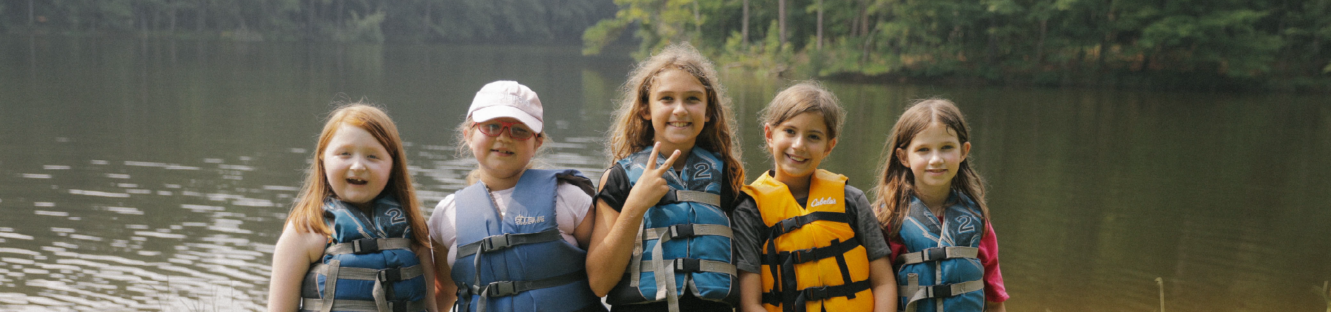  young Girl Scouts in life jackets pose for photo near a lake 