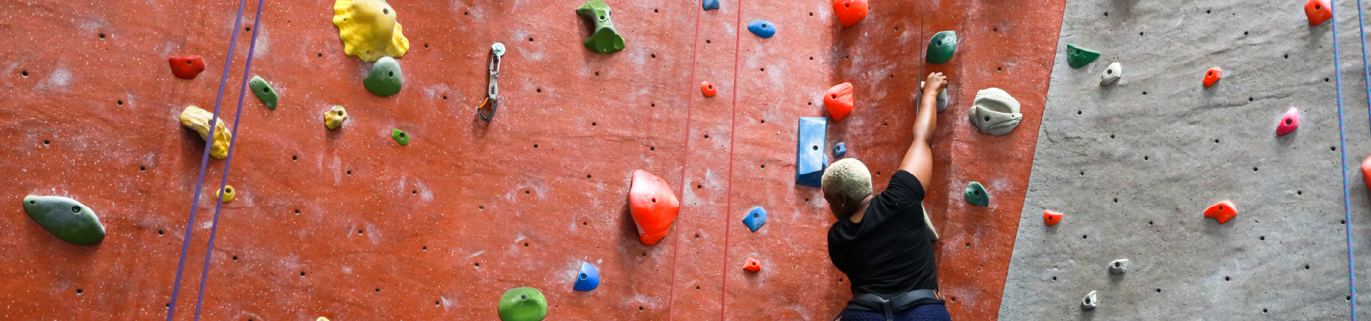  girl wearing a black shirt with harness climbs on red indoor rock wall 